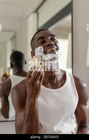 Crema da barba per metà adulto, uomo afro-americano, in un bagno moderno con spazzola e spazio fotocopie Foto Stock