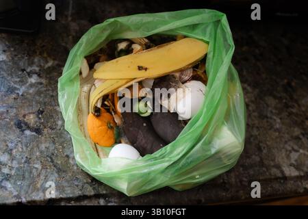 Vari scarti di frutta e verdura raccolti in un sacchetto verde sono collocati su un ripiano della cucina in granito. Foto Stock