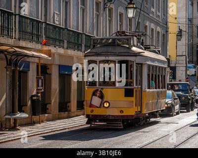 Un classico tram giallo percorre una strada soleggiata nel cuore di Lisbona, in Portogallo, circondata da un'affascinante architettura e da una vivace vita cittadina Foto Stock