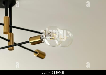 Elegante lampadario con lampadine a incandescenza a vista, su sfondo bianco luminoso, che mette in mostra moderne apparecchiature di illuminazione e design degli interni Foto Stock