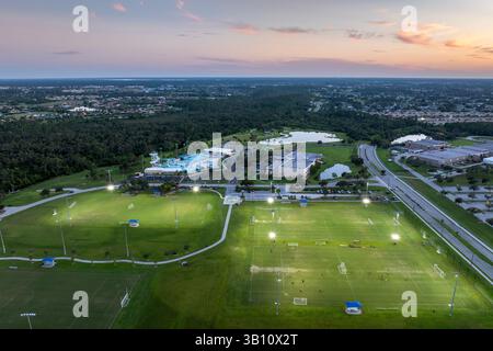 Arena sportiva pubblica illuminata a North Port, Florida, con persone che giocano una partita di calcio sullo stadio di calcio in erba al tramonto. Concetto di attività all'aperto Foto Stock