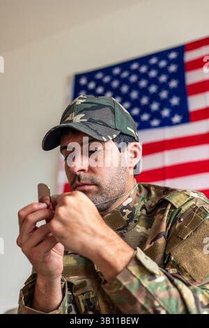 Depresso veterano militare che tiene il dog tag con la bandiera degli Stati Uniti sullo sfondo, soffre di disturbo da stress post-traumatico, problema psicologico Foto Stock