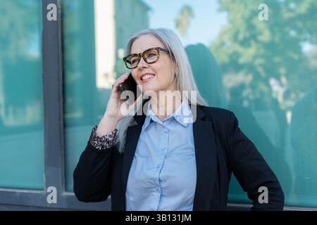 Un'elegante donna d'affari parla con fiducia sul suo smartphone, mostrando il suo carattere e la sua professionalità Foto Stock
