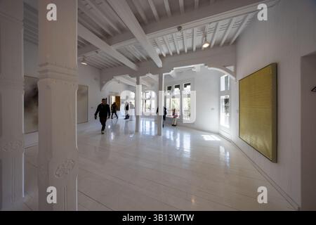 I visitatori camminano attraverso una sala luminosa del Museo de Arte Abstracto Español a Cuenca, Castilla-La Mancha, Spagna, con travi in legno dipinti di bianco sul soffitto. Un dipinto astratto giallo oro è appeso alla parete di destra, e la luce del giorno filtra attraverso le finestre sullo sfondo sul pavimento in legno lucido. Colonne in pietra con capitelli floreali strutturano la stanza. Calle Canónigos, Cuenca, Castilla-La Mancha, Spagna. Foto Stock
