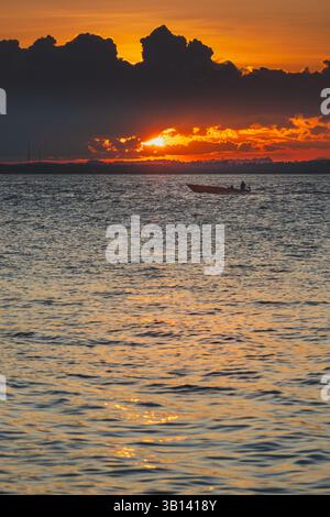 Un vibrante tramonto sulla baia di Balikpapan, caratterizzato da una piccola barca che si staglia contro il cielo arancione ardente e le nuvole scure e spettacolari. Foto Stock