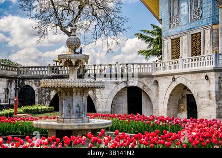 Fontana circondata da tulipani rossi in fiore di fronte al chiosco ornato di Baghdad con piastrelle blu e bianche nel Palazzo Topkapi. Istanbul, Turchia-Turkiye Foto Stock