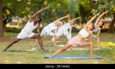Persone di età e nazionalità diverse praticano varie pose yoga nel giardino estivo Foto Stock