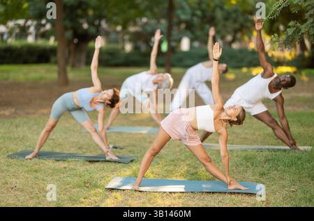 Persone di età e nazionalità diverse praticano varie pose yoga nel giardino estivo Foto Stock