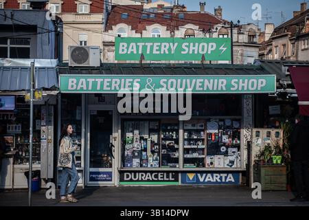 BELGRADO, SERBIA - 21 MARZO 2025: Negozio di batterie con vetrina intonacata con segnaletica verde vende batterie, riparazioni telefoniche e souvenir; fornisce Foto Stock