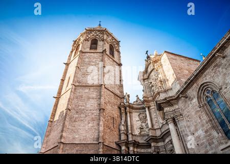 Vista dal basso angolo del portale principale barocco della Cattedrale di Valencia e del campanile Miguelete che si illumina in tarda luce del sole contro un cielo mediterraneo blu profondo in spagna Foto Stock