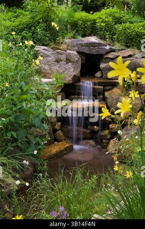 Cascata artificiale in pietra naturale con margherite gialle Hemerocallis - gialli, Leucanthemum x superbum - margherite Shasta nel giardino di campagna in estate. Foto Stock
