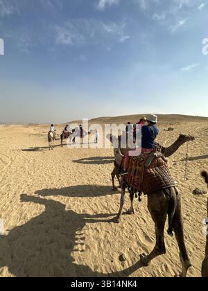 Giza, Egitto - 19 ottobre 2023: Giro turistico a dorso di cammello intorno alle piramidi di Giza in una giornata di sole Foto Stock