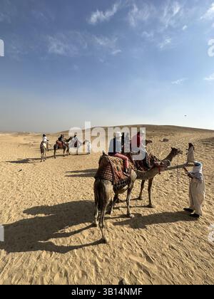 Giza, Egitto - 19 ottobre 2023: Giro turistico a dorso di cammello intorno alle piramidi di Giza in una giornata di sole Foto Stock