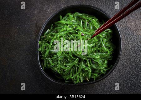 Insalata Chuka, preparata con alghe fresche, con condimento di sesamo, servita in una ciotola nera, con bacchette Foto Stock
