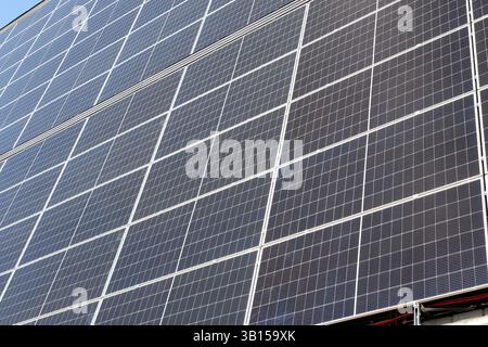 Ampia gamma di pannelli solari installati sul lato di un edificio, che riflettono la luce solare. Le strutture di supporto e il cablaggio elettrico sono visibili. Foto Stock