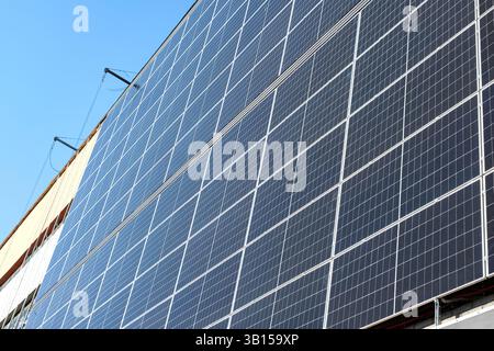 Montaggio di una vasta gamma di pannelli solari sul lato di un edificio. Verricelli, strutture di supporto e cablaggio elettrico sono visibili. Foto Stock