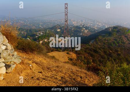 Scatto grandangolare che cattura il paesaggio panoramico di Los Angeles dal Runyon Canyon Park, caratterizzato da un terreno accidentato e da un'importante torre di potere contro un Foto Stock