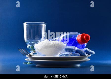 Dettaglio dei prodotti per lavastoviglie con stoviglie come piatti, posate e bicchieri isolati su sfondo blu. Vista frontale. Foto Stock