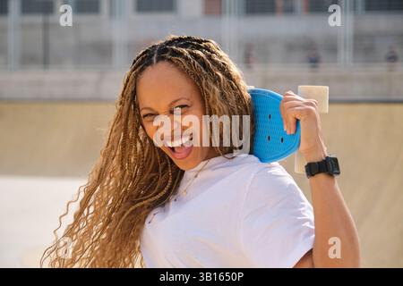 Skater entusiasta che tiene in mano il penny board blu che ride nello skate Park Foto Stock