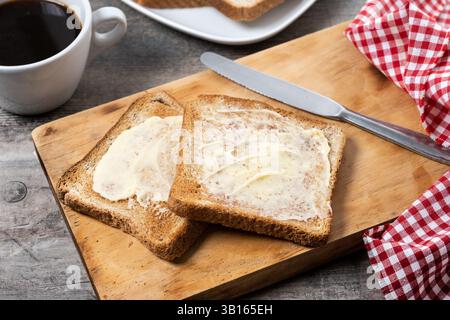 Affettare pane fresco e burro su un tavolo di legno Foto Stock