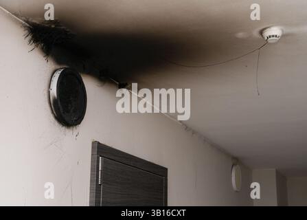 Lampada LED bruciata. Una lampada a paralume sulla parete dopo un incendio. Combustione spontanea e incendio in un edificio residenziale. Sensore di allarme antincendio interno. Fumo nero Foto Stock