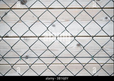 Una recinzione a maglie a catena è posizionata direttamente contro una robusta parete in legno, creando un contrasto tra i due diversi materiali utilizzati nella costruzione Foto Stock