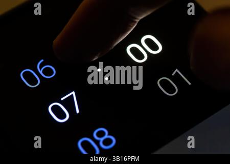 Impostazione con le dita della sveglia digitale dello smartphone alle 7:00 in una stanza buia di notte, moderno telefono cellulare. Sveglia programmata, orario di sveglia mattutina con Foto Stock