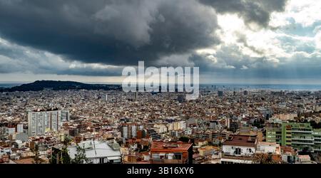 Una vista panoramica di un'estesa città sotto un cielo spettacolare pieno di nuvole scure e raggi di luce solare che si infrangono. Il paesaggio urbano è caratterizzato da un mix Foto Stock