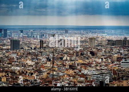 Una vista panoramica di un vasto paesaggio urbano sotto un cielo nuvoloso, con raggi di luce del sole che si infrangono tra le nuvole. Il paesaggio urbano presenta un mix di Foto Stock