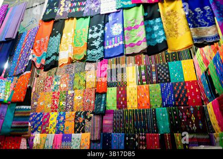 Betel Leaves display Zegyo Market Mandalay Myanmar // MANDALAY, Myanmar — le foglie di Betel sono impilate con cura e disposte in un modello circolare presso la bancarella di un fornitore nel mercato di Zegyo. Queste fresche foglie verdi del vitigno Piper betle servono da involucro per il liquido di betel (noto localmente come kun-ya), un leggero stimolante ampiamente consumato in Myanmar. La meticolosa disposizione riflette sia considerazioni pratiche per mantenere la freschezza che i valori estetici tradizionali negli schermi di mercato. I venditori di betel in genere vendono non solo le foglie, ma anche altri ingredienti necessari per la preparazione del liquido, Foto Stock