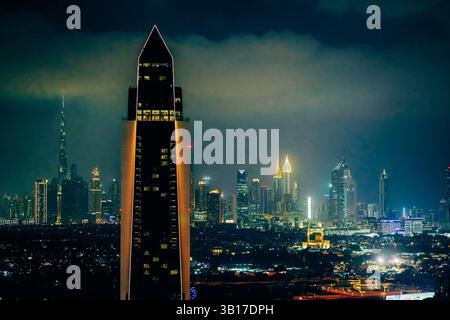 Lo skyline di Dubai illuminato di notte, con il Burj Khalifa e altri grattacieli di rilievo sotto un cielo spettacolare e nuvoloso. Foto Stock