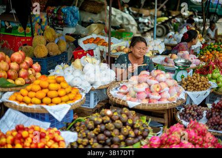 Vendor di frutta e verdura del mercato Zegyo Mandalay Myanmar | MANDALAY, Myanmar — Una venditrice sistema melagrane, durian, mele e altra frutta al suo banco nel mercato all’aperto di prodotti agricoli che circonda il mercato Zegyo, considerato la sezione più caratteristicamente birmana del distretto commerciale. Contadini e mercanti portano qui prodotti stagionali dalla fertile pianura superiore dell’Irrawaddy, una relazione di approvvigionamento che risale alla fondazione del mercato sotto il re Mindon negli anni ’50 dell’Ottocento. Zegyo funziona principalmente come hub di vendita all’ingrosso e semi-ingrosso, servendo acquirenti domestici e commercianti che ridistribuiscono i prodotti agricoli in U Foto Stock