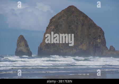 CANNON BEACH, OREGON, USA - 12 aprile 2025: Le iconiche formazioni rocciose alte di Cannon Beach si stagliano sullo sfondo di un cielo nuvoloso. Foto Stock