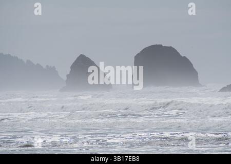 CANNON BEACH, OREGON, USA - 12 aprile 2025: Le iconiche formazioni rocciose alte di Cannon Beach si stagliano sullo sfondo di un cielo nuvoloso. Foto Stock