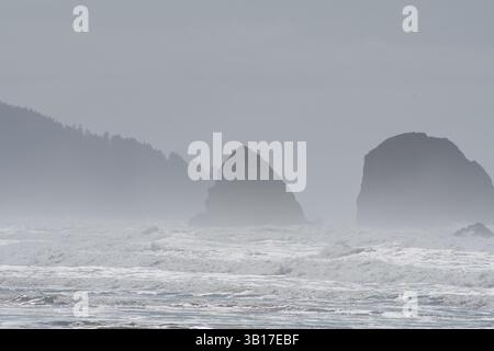 CANNON BEACH, OREGON, USA - 12 aprile 2025: Le iconiche formazioni rocciose alte di Cannon Beach si stagliano sullo sfondo di un cielo nuvoloso. Foto Stock