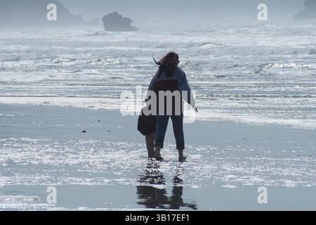 CANNON BEACH, OREGON, USA - 12 aprile 2025: I visitatori camminano lungo le spiagge sabbiose di Cannon Beach sotto un cielo nuvoloso, con l'iconica Haystack Rock in piedi. Foto Stock