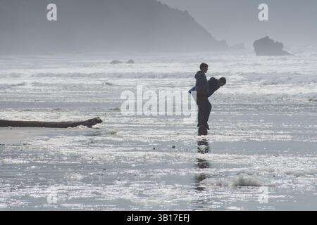 CANNON BEACH, OREGON, USA - 12 aprile 2025: I visitatori camminano lungo le spiagge sabbiose di Cannon Beach sotto un cielo nuvoloso, con l'iconica Haystack Rock in piedi. Foto Stock