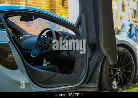 Un'elegante auto sportiva McLaren blu con portiera aperta che mostra gli interni e il volante, parcheggiata all'aperto. Foto Stock