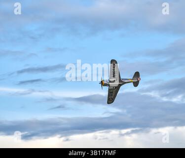 Un aeroplano d'epoca dell'esercito degli Stati Uniti d'America color argento e giallo sorvola un cielo azzurro pallido con nuvole bianche sparse. Foto Stock