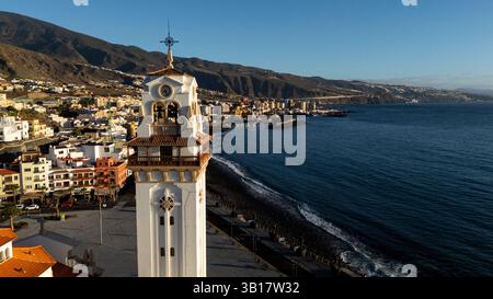 Un'alta torre bianca con un orologio in cima sorge di fronte a una città con una splendida vista sull'oceano Foto Stock