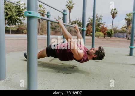 Un uomo sta facendo pull up australiani facendo il suo allenamento fuori, foto orizzontale. Foto Stock
