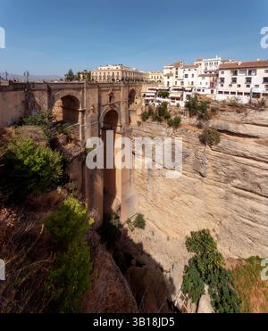 Vista del ponte Puente Nuevo sulla gola di El Tajo a Ronda, Andalusia, Spagna, con edifici storici e scogliere spettacolari sotto un cielo limpido. Foto Stock