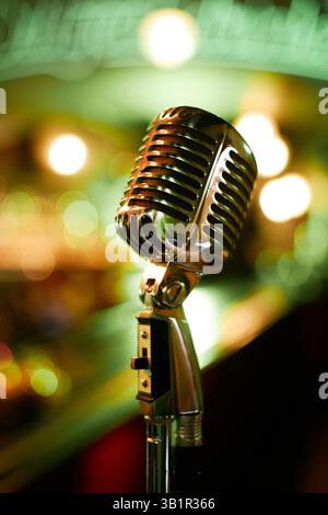 Primo piano verticale su un vecchio microfono cromato catturato contro luci al neon sfocate di colore verde nel jazz club, spazio copia Foto Stock