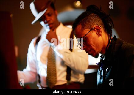 Vista laterale del musicista maschile di etnia mista che indossa occhiali che suona il pianoforte con precisione professionale mentre esegue musica dal vivo nel jazz club sotto una calda luce ambientale, spazio fotocopie Foto Stock