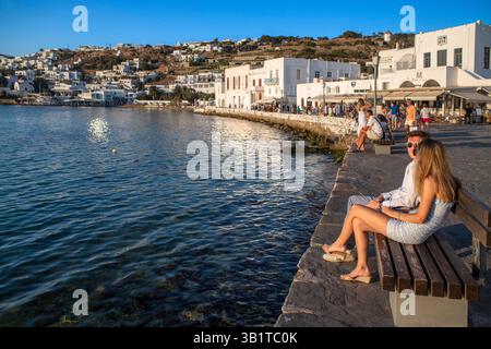 Coppia turistica sul lungomare di Mykonos e paesaggio urbano al tramonto, Cicladi, Grecia. Mykonos è un'isola greca, parte delle Cicladi, situata tra T Foto Stock