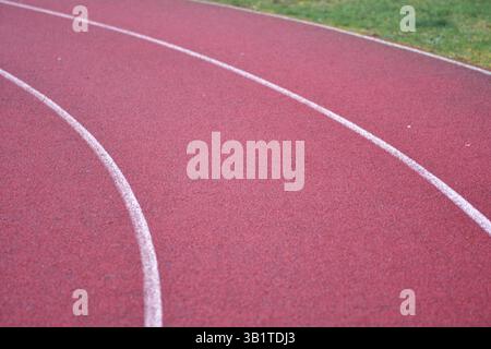 curva rossa della pista da corsa con linee bianche e erba verde sul lato destro Foto Stock