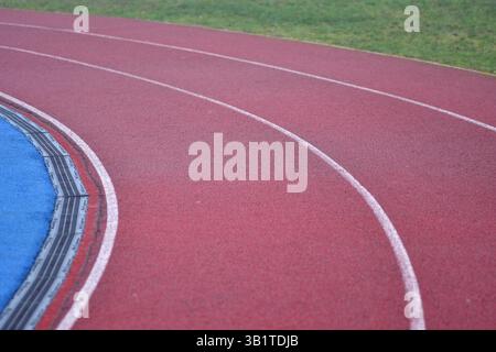 curva rossa della pista da corsa con linee bianche, campo sportivo blu sul lato sinistro e erba verde sul lato destro Foto Stock