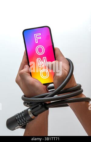 Le mani sono bloccate con un blocco del cavo, tenendo in mano uno smartphone con FOMO (paura di perdere): Dipendenza dai social media, paura di perdere qualcosa Foto Stock
