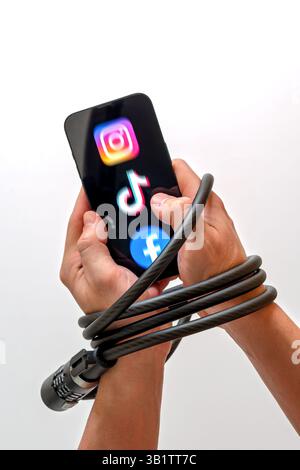 Le mani sono bloccate con un blocco cavo, tenendo uno smartphone con logo Instagram, Tik-Tok e Facebook. Foto Stock