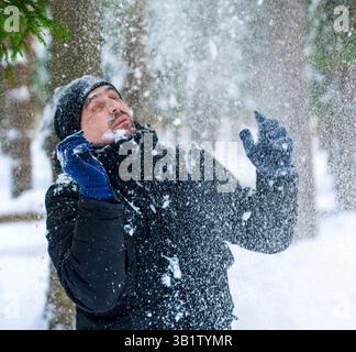 Uomo che strizza mentre la neve cade pesantemente dagli alberi nella foresta invernale Foto Stock